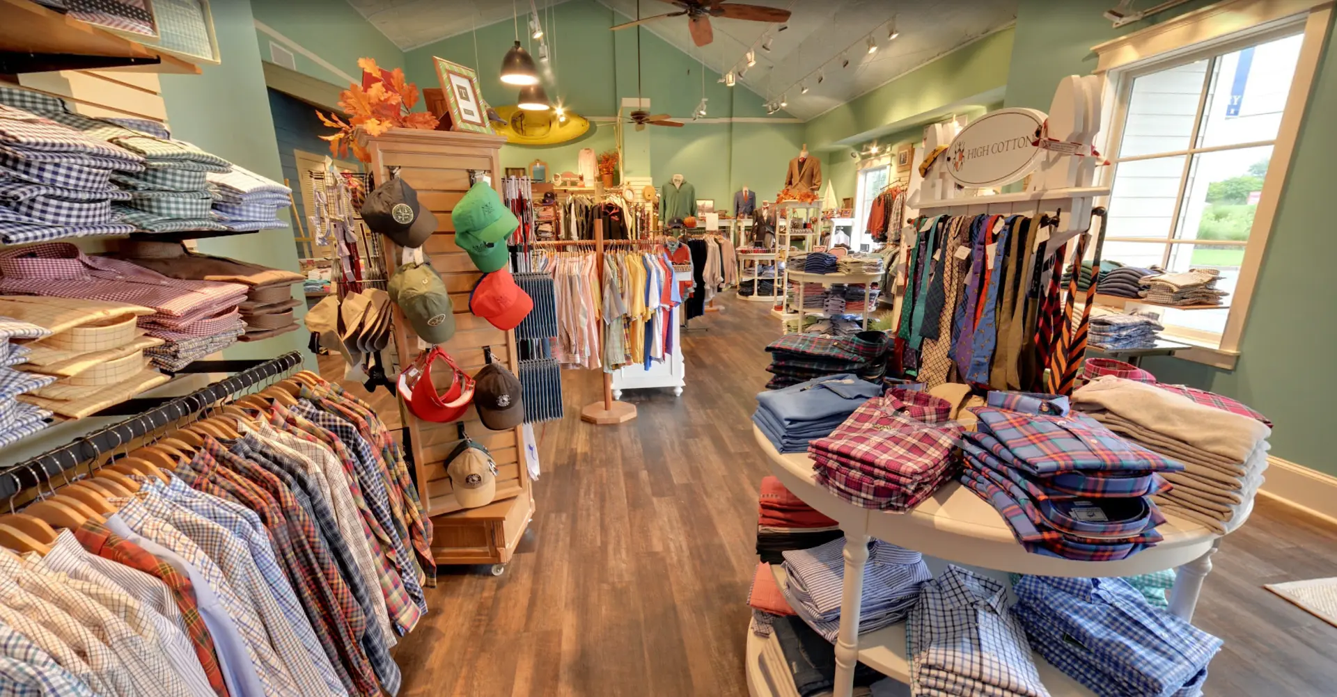 Inside Low Country Clothier: stacked sport shirts, hats, and racks of tailored clothing along the store aisle