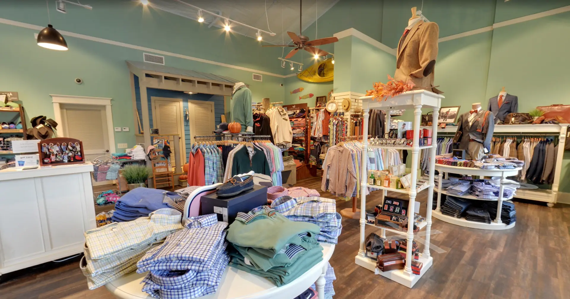 Inside Low Country Clothier: folded shirts and sweaters on a display table with racks of tailored clothing beyond